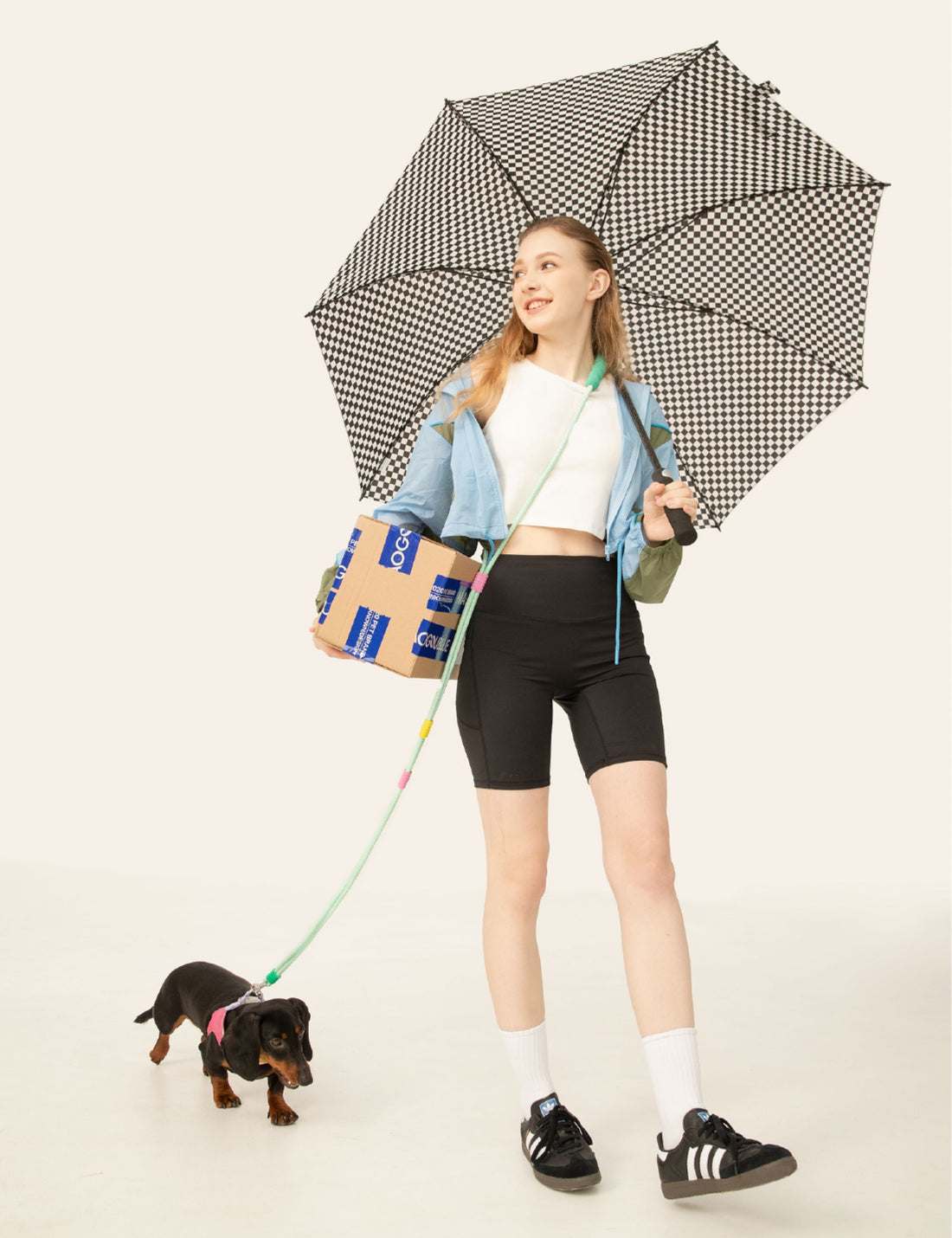 Young woman walking small dog with UNIPATS colorful dog leash and umbrella in a bright studio scene1621243260e1af0c20-0
